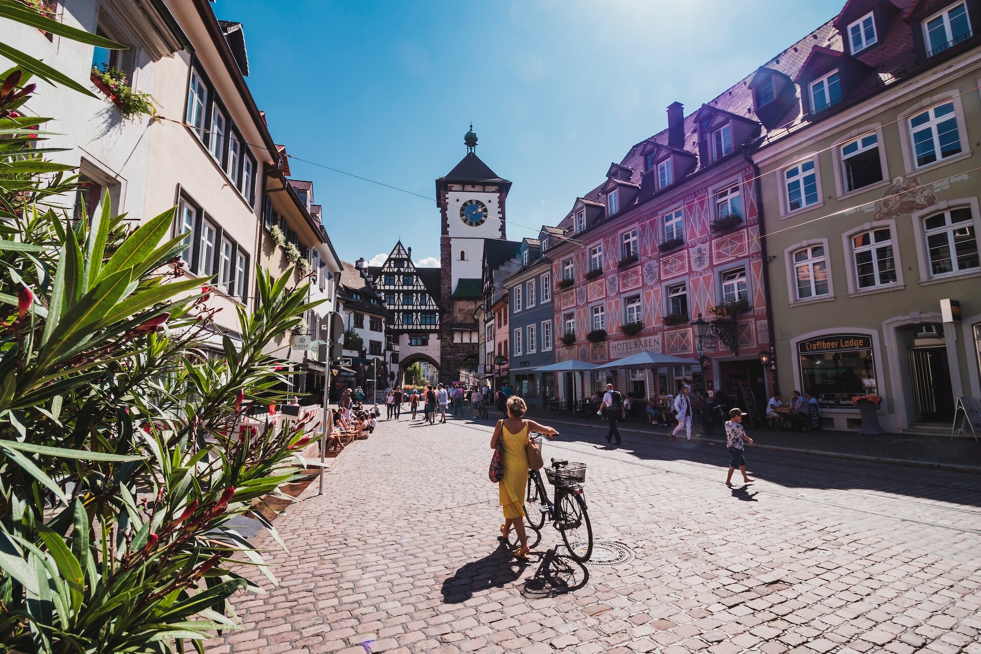 Eine Frau im gelben Kleid schiebt ihr Fahrrad durch die Freiburger Altstadt an einem sonnigen Tag